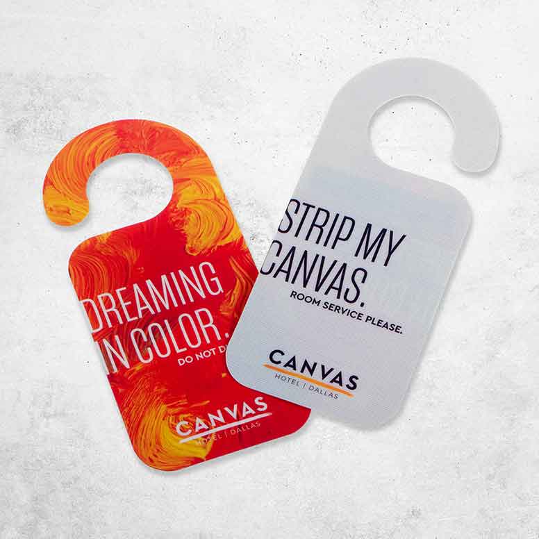 Two colorful hotel door hangers: one red/orange with Dreaming in Color, one white with Strip My Canvas.