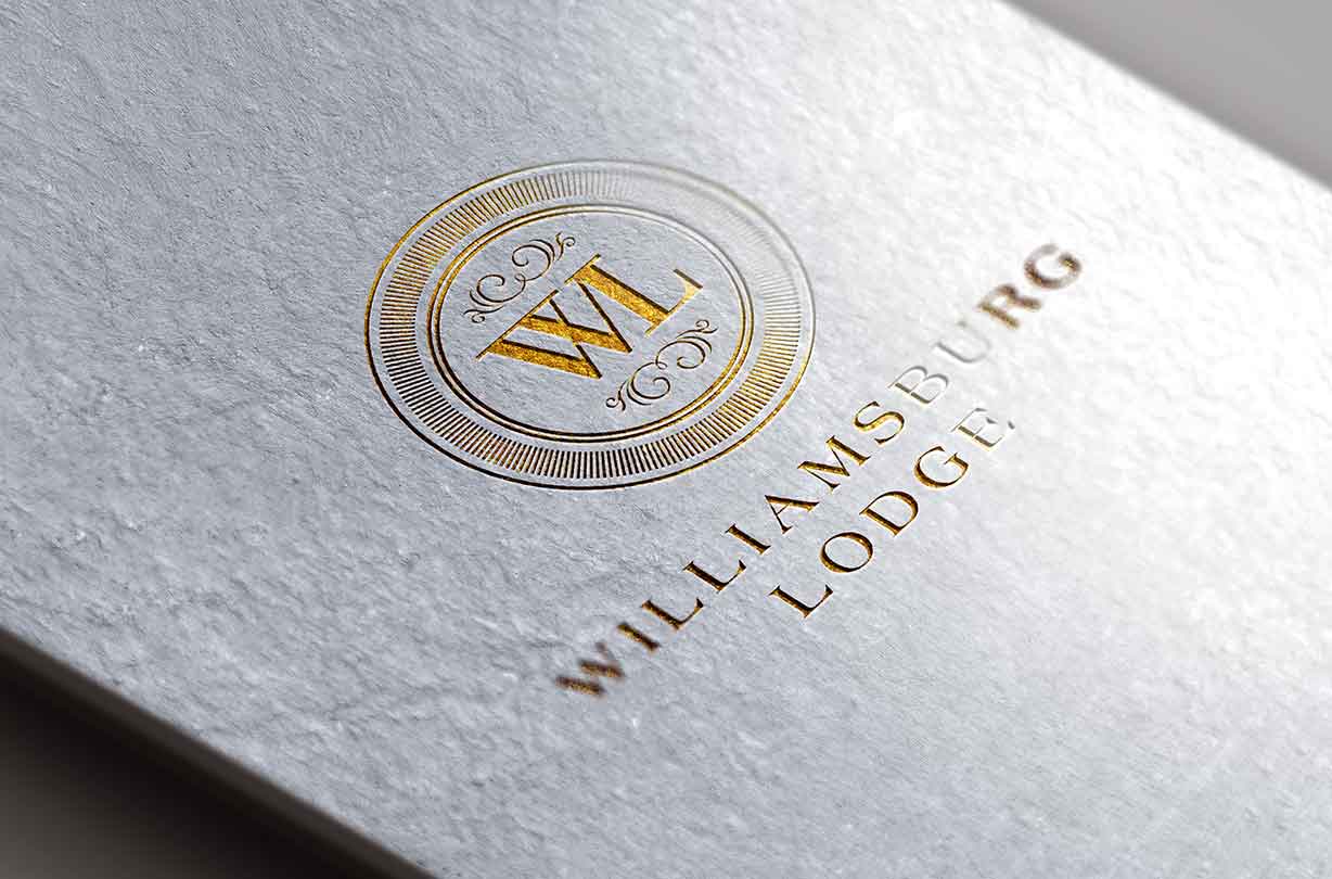 Gold embossed Williamsburg Lodge logo on textured white paper, featuring “WL” in a circular emblem.