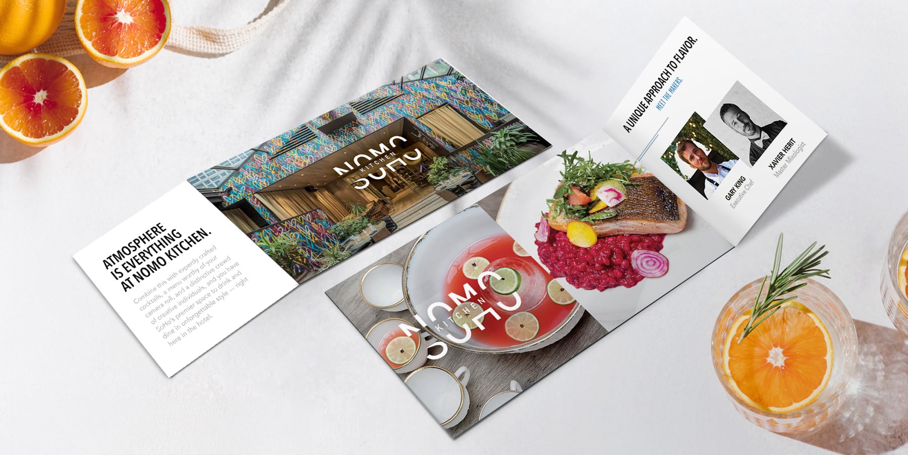 A brochure with dishes, drinks, and restaurant info, surrounded by sliced oranges and a drink with rosemary.