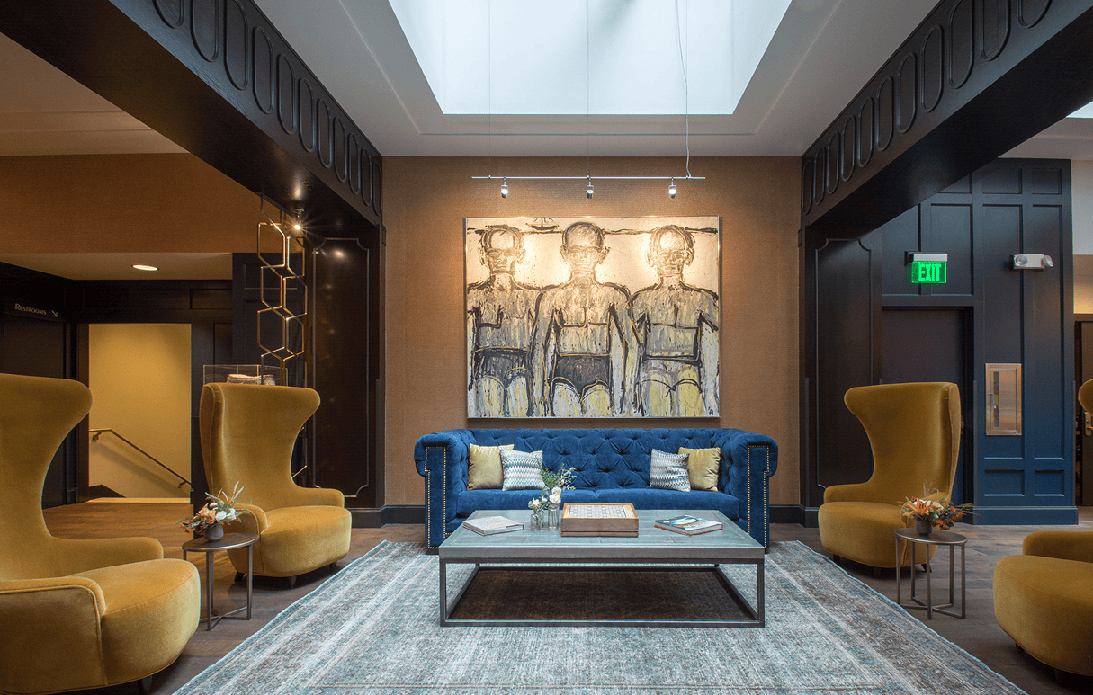 Modern lounge with a blue sofa, mustard chairs, abstract art, and a large skylight overhead.