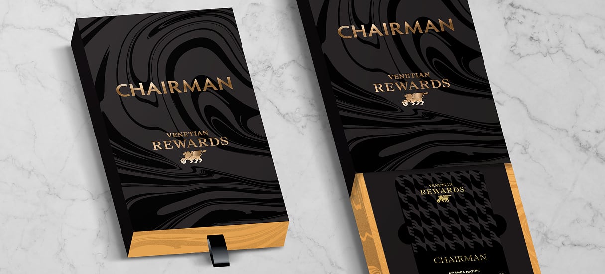 Two black and gold Chairman Venetian Rewards boxes with a marble pattern, displayed on a marble surface.