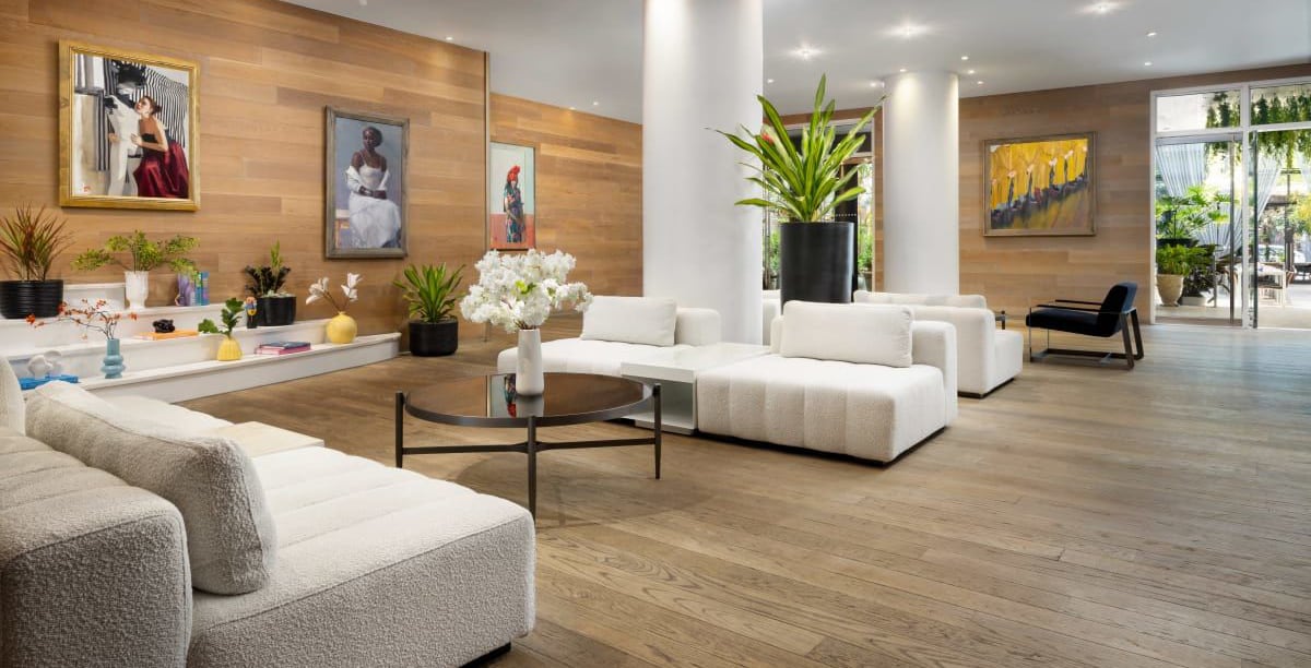 Modern lobby with white sofas, wooden floors, large plants, and colorful artwork on the walls.
