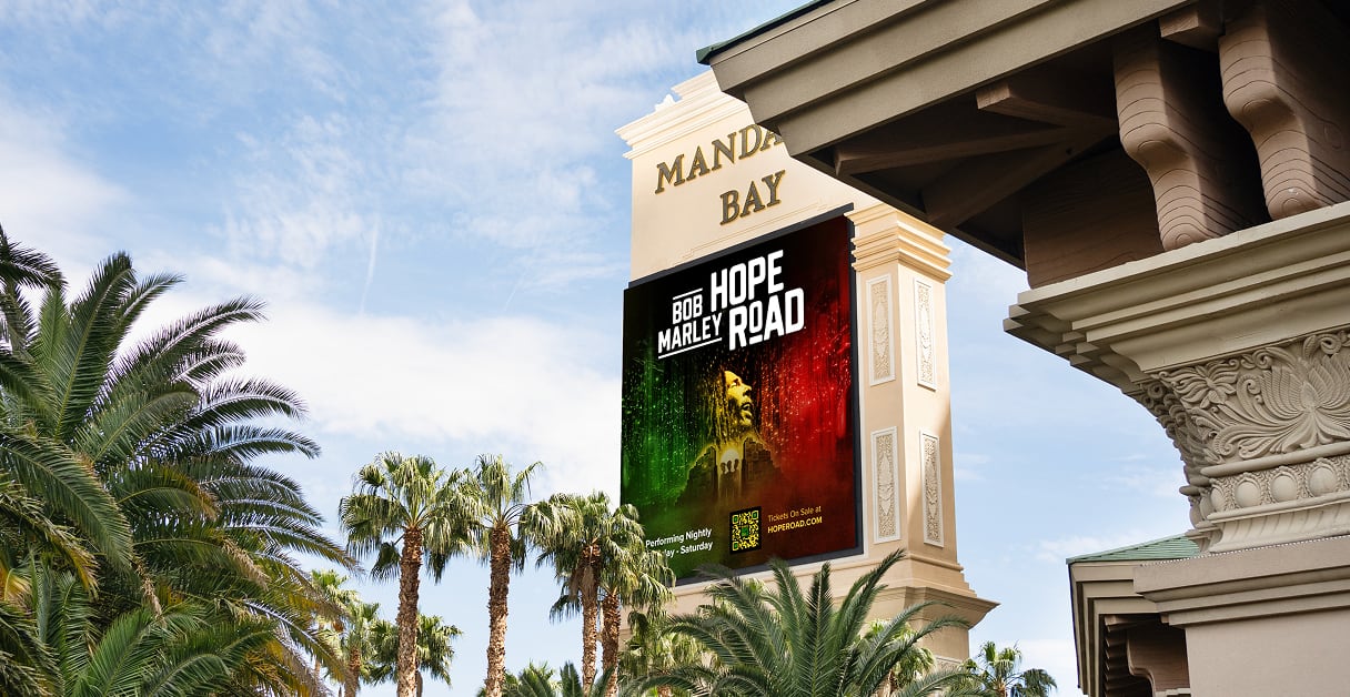 A large Bob Marley Hope Road poster on the Mandalay Bay sign, surrounded by palm trees and blue sky.